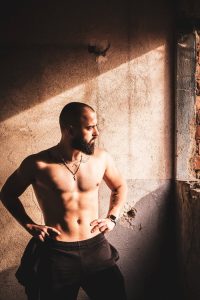 Muscular man standing shirtless, showcasing fitness in dramatic light.