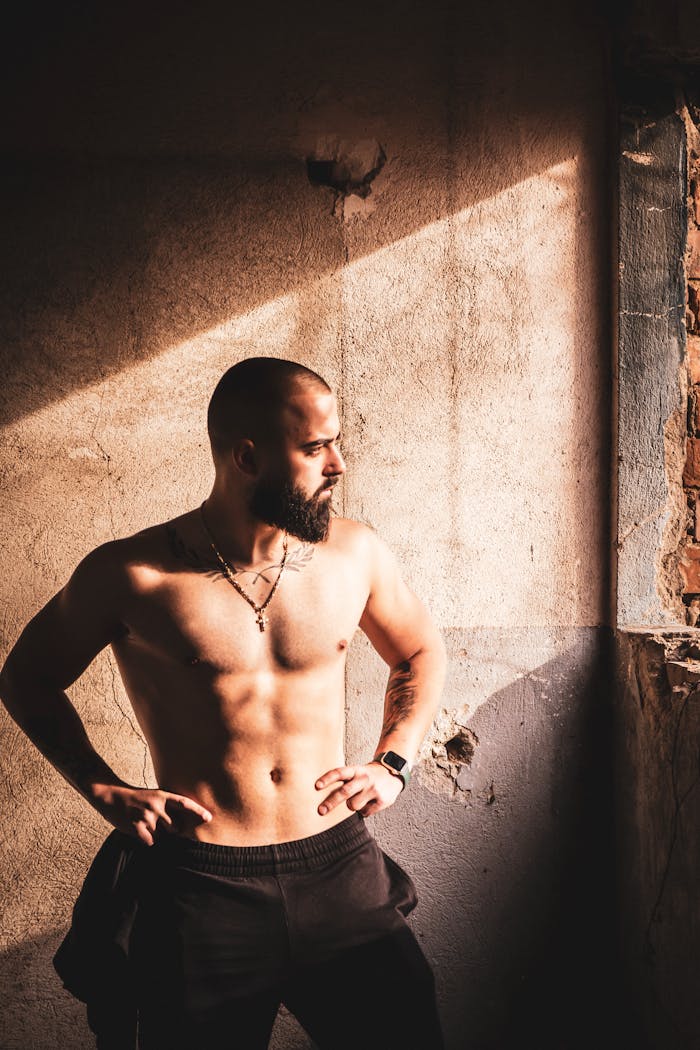 Muscular man standing shirtless, showcasing fitness in dramatic light.
